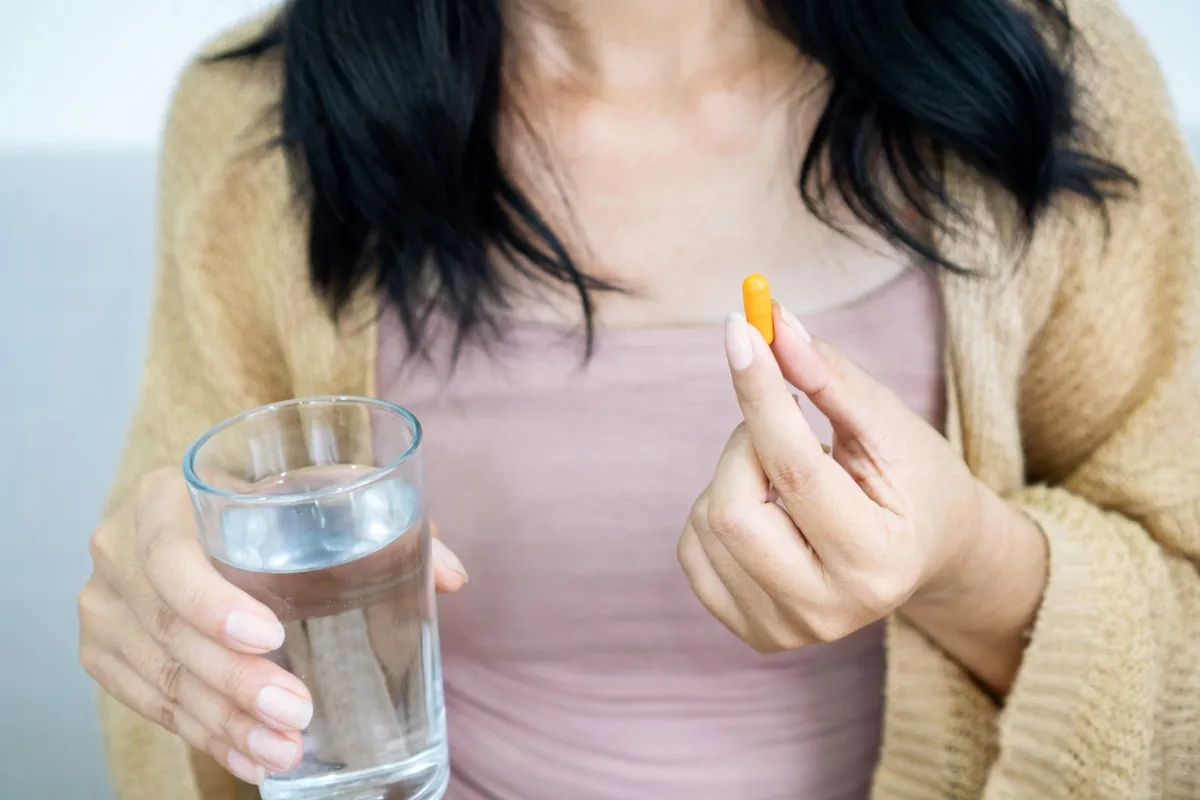 Woman's hand taking turmeric pill, girl's hand holding turmeric powder in capsule or curcumin herbal medicine with a glass of water, acid reflux problem treatment