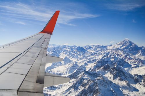 View of an airplane wing over snow capped mountains.