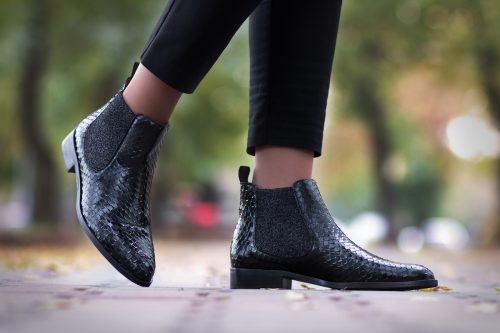 Close up of a woman's legs walking along the street in black python ankle boots.
