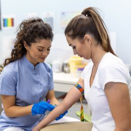 Preparation for blood test with pretty young woman by female doctor medical uniform on the table in white bright room. Nurse pierces the patient's arm vein with needle blank tube.