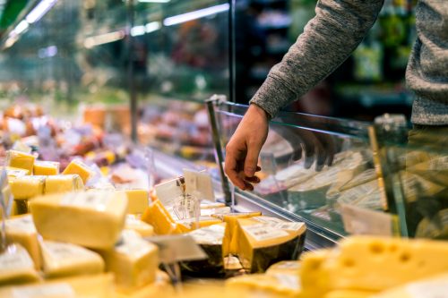 A close up of someone's hand as they take cheese out of a display case at a supermarket