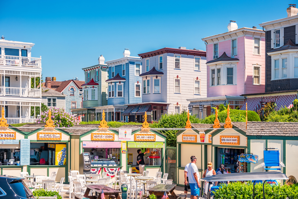 People browse vendor booths in downtown Cape May, New Jersey on a sunny summer day with colorful Victorian homes in the background.