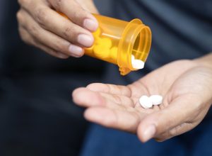 A close up of hands holding a prescription bottle and medication