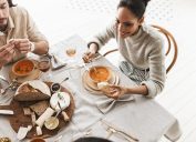 Top view of a couple dressed in neutrals eating soup, along with bread and cheese.