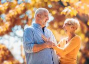 An older couple holding each other and laughing with autumn leaves behind them.