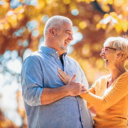An older couple holding each other and laughing with autumn leaves behind them.