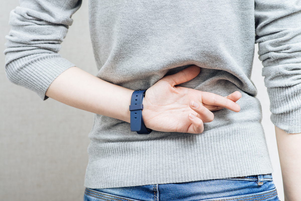 Close up of a woman's back in a gray sweater with her fingers crossed behind her back.
