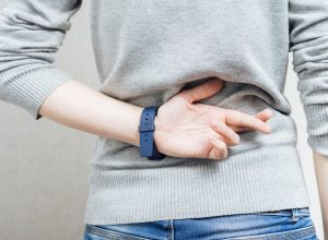 Close up of a woman's back in a gray sweater with her fingers crossed behind her back.