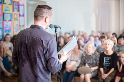 man reading an excerpt from a book in front of a crowd