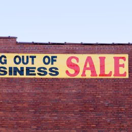 A "going out of business" sale sign hanging on the side of a brick building