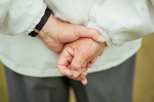 A close up shot of a senior man's hands behind his back, holding them together.