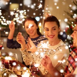 A group of happy friends at a dinner table celebrating the holidays with sparklers.