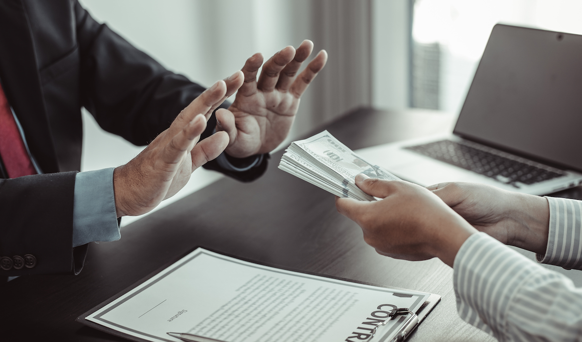Close up of a businessman's hands refusing money from another set of hands.