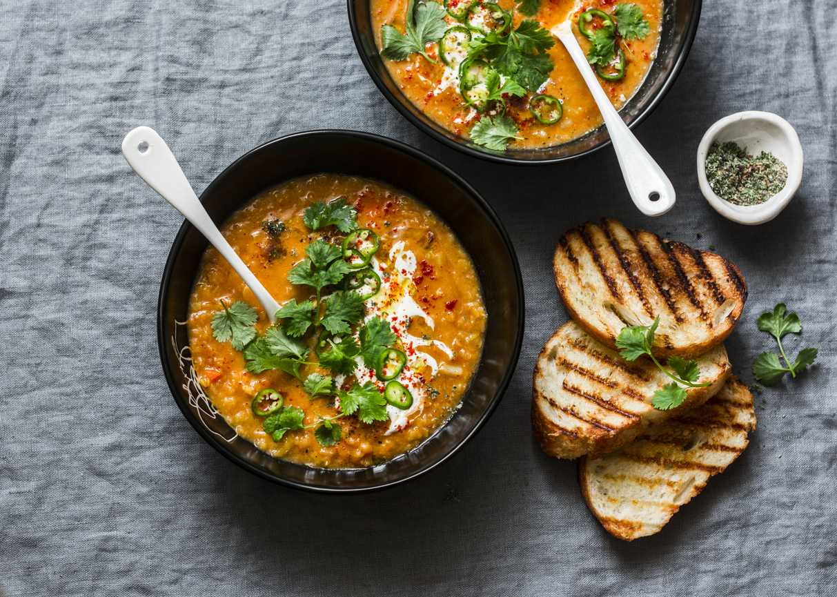 Curried red lentil tomato and coconut soup in two bowls with grilled bread on gray background