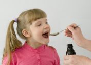 Smiling girl taking medication from a spoon.