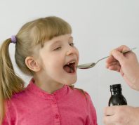 Smiling girl taking medication from a spoon.
