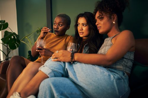 Shot of three friends having snacks and drinks while enjoying a movie night