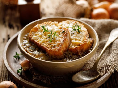 Traditional French onion soup baked with cheese croutons sprinkled with fresh thyme, close-up.