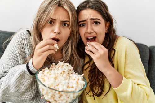 Young couple scared watching horror film eating popcorn at home.
