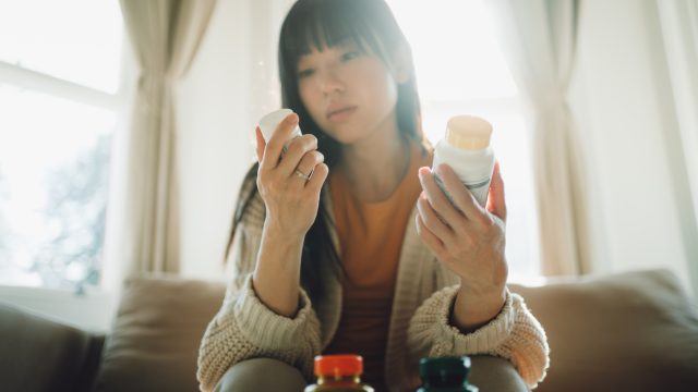 Woman looking at pill and holding medication container.