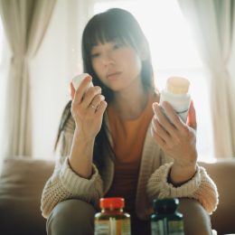 Woman looking at pill and holding medication container.