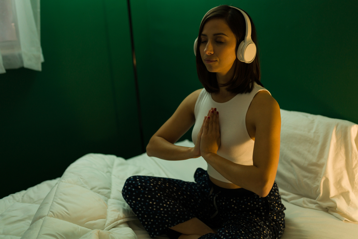 Woman meditating and listening to headphones on a bed.