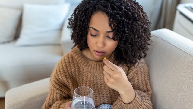 Woman on couch taking medication with a glass of water.