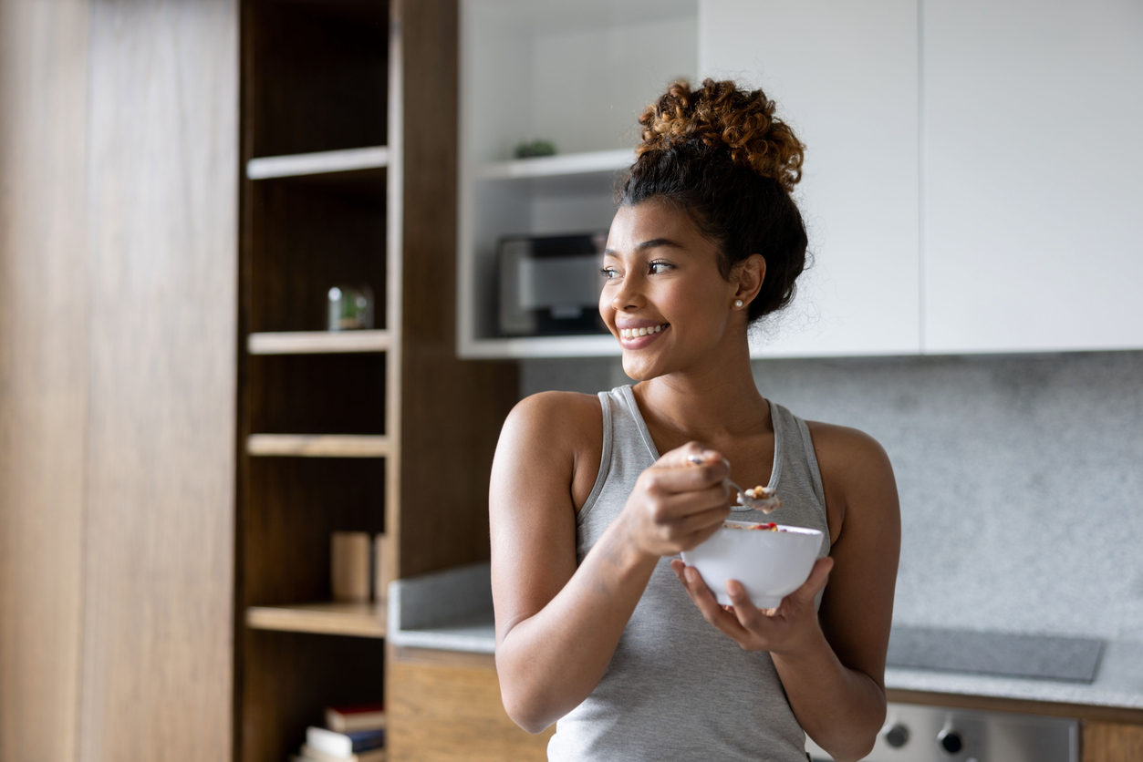 Woman eating yogurt in a kitchen.