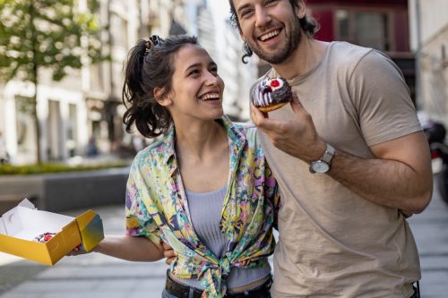 Young couple outdoors, enjoying donuts