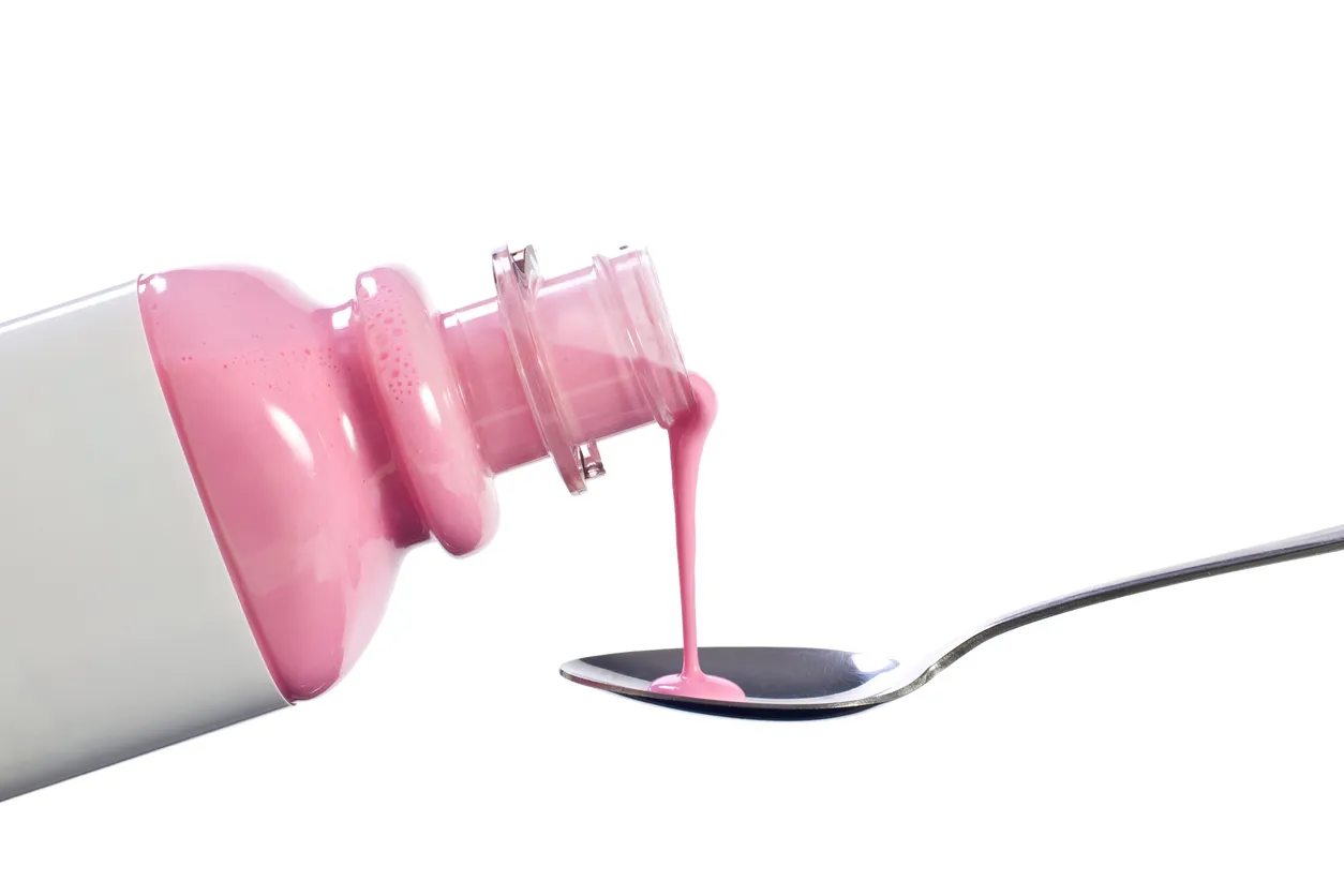 Pink medicine is poured into a spoon.