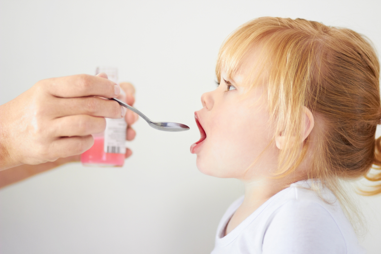 Little girl being administered pink medicine.