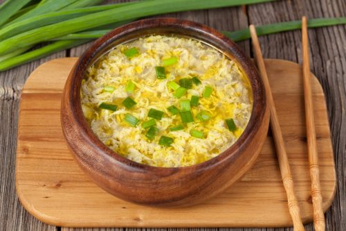 Vegetarian traditional asian drop egg soup with broth in wooden bowl on vintage background