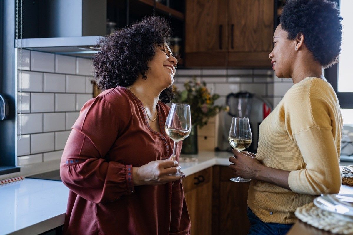 Two women talking in the kitchen and drinking white wine