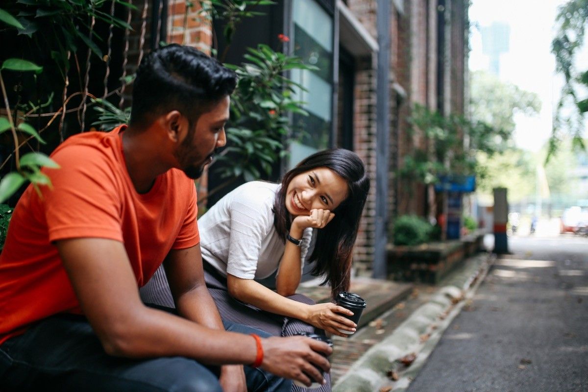 Young people talking and flirting on the streets of Kuala Lumpur, having a coffee break together in front of their office or university library.