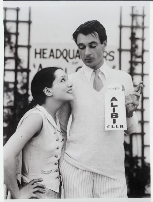 Lupe Vélez and Gary Cooper posing for a photo as Cooper holds an "Alibi Club" sign