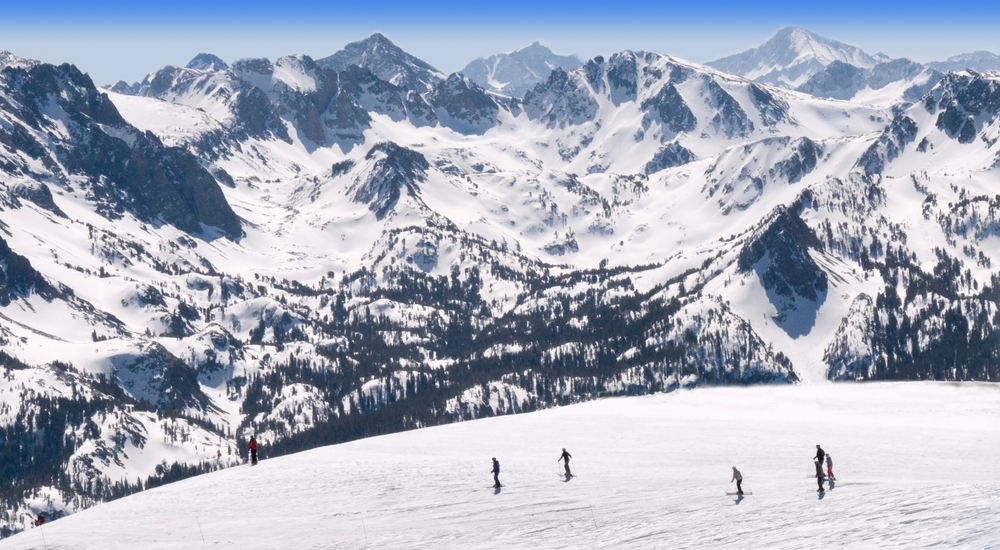 A group of skiers standing on top of a trail on Mammoth Mountain with peaks in the background
