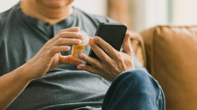 Close up of a man looking at his medication bottle while using his phone