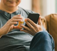 Close up of a man looking at his medication bottle while using his phone