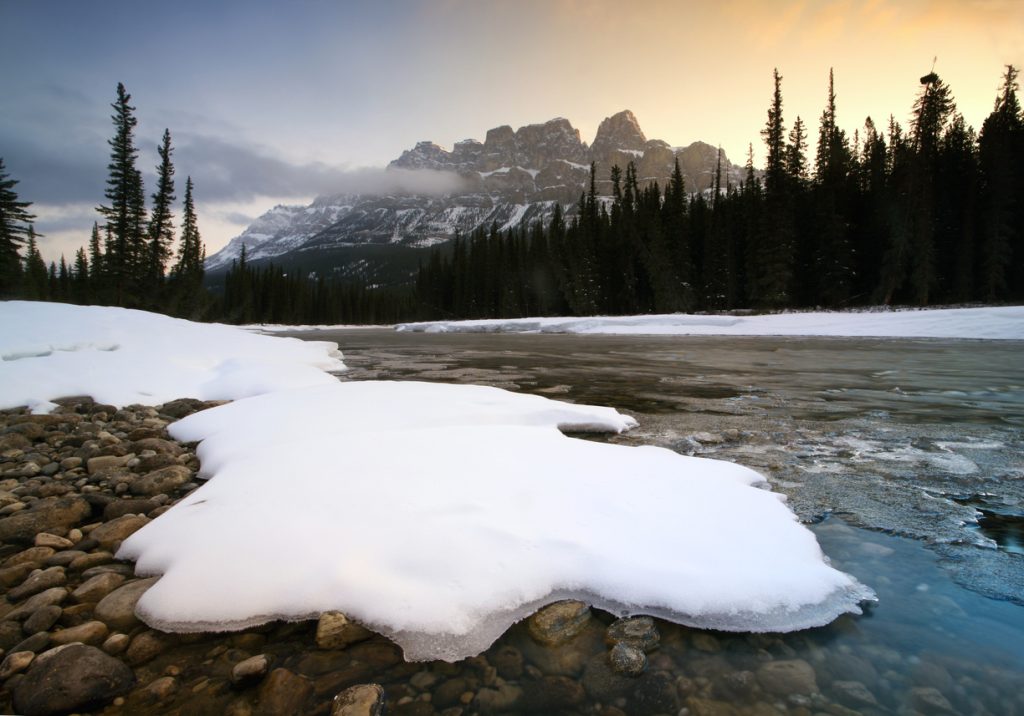 Snow melting on a riverbank with the Canadian Rockies in the background