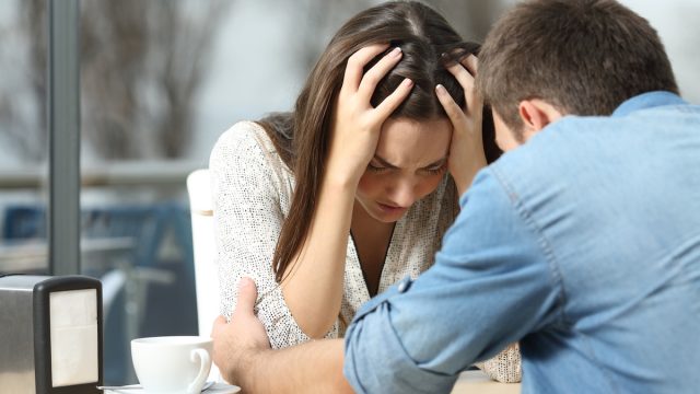 A man comforting his needy, sad female partner at a restaurant table.