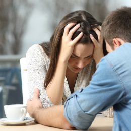 A man comforting his needy, sad female partner at a restaurant table.