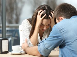 A man comforting his needy, sad female partner at a restaurant table.