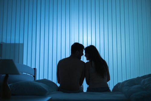 man and woman sitting close on bed at night