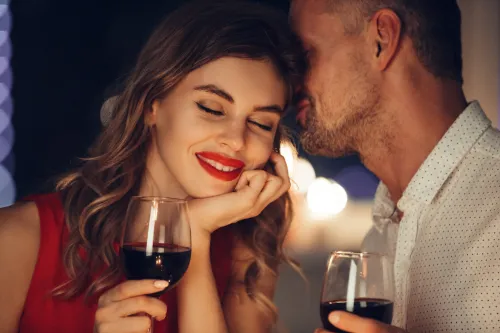 man whispering to his girlfriend while drinking red wine