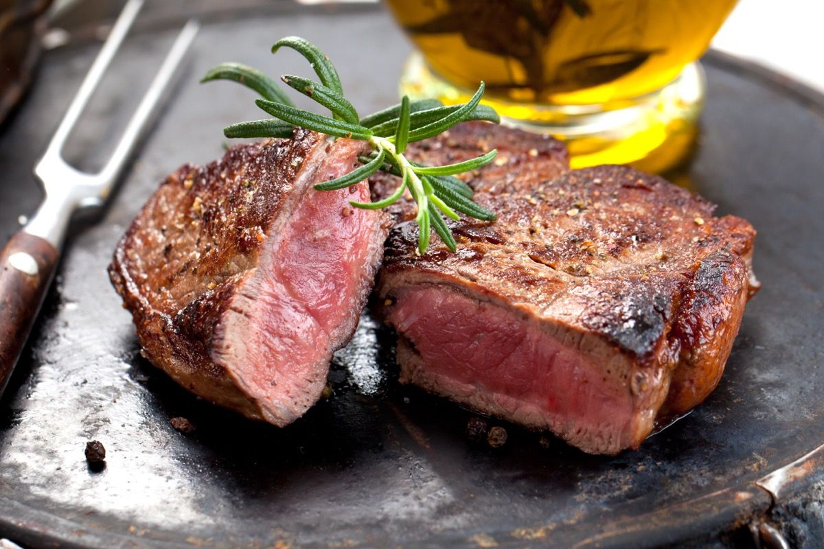 Cooked Steak cut in half on a plate with a piece of rosemary