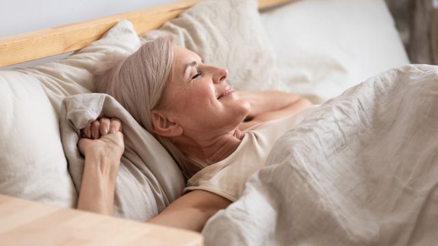 Satisfied middle aged woman lying in bed enjoy early morning