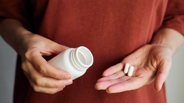 A woman pours pills or vitamins from a jar onto her hand. Taking vitamins or medications. The concept of health care, medicine, pharmacies, disease prevention. A jar with pills or vitamins in the hand