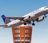 A United Airlines flight taking off from the airport with an air traffic control tower in the background