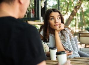 A bored-looking young woman sits at the table having a coffee with a man.