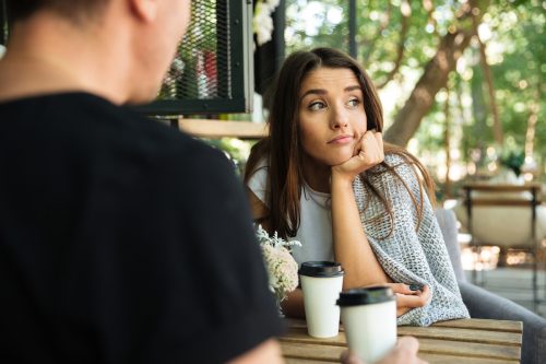 A bored-looking young woman sits at the table having a coffee with a man.